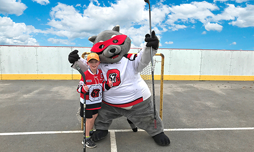 Riley Racoon posing with a young fan in front of a street hockey net