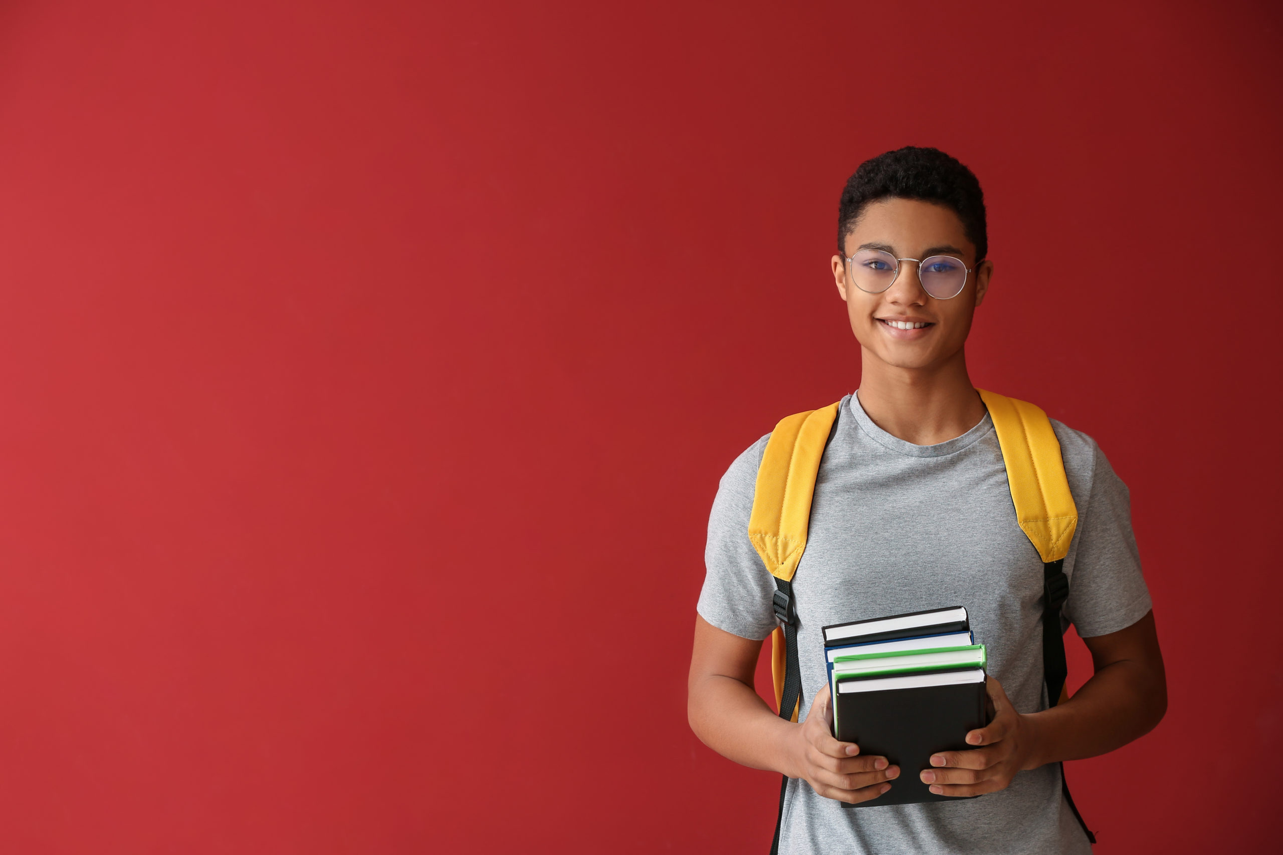 College male Student with glasses, grey shirtholding books . Red background